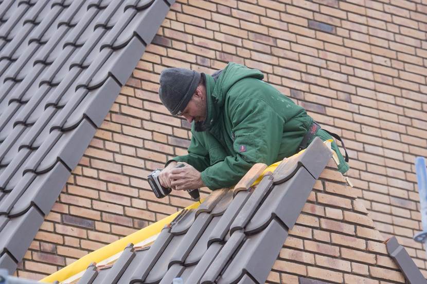 man werkt op het dak met een schroefboormachine